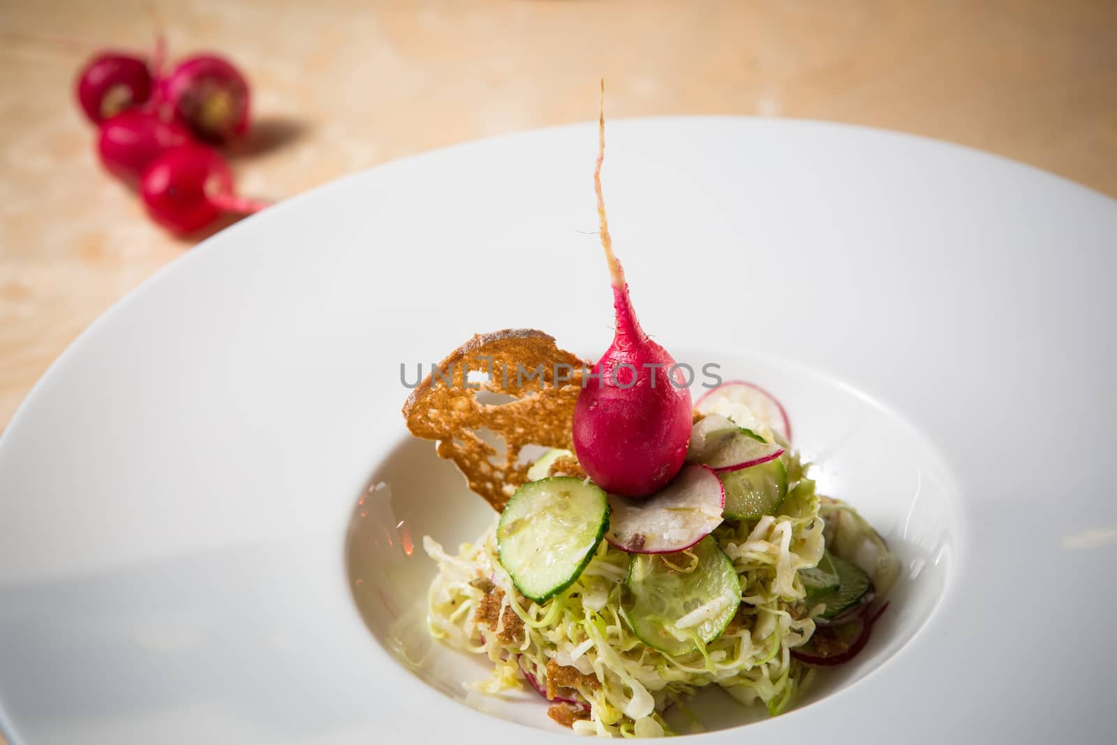 Salad from cabbage, herbs, cucumber, onion and radish in bowl on green wooden background. Coleslaw. Selective focus.