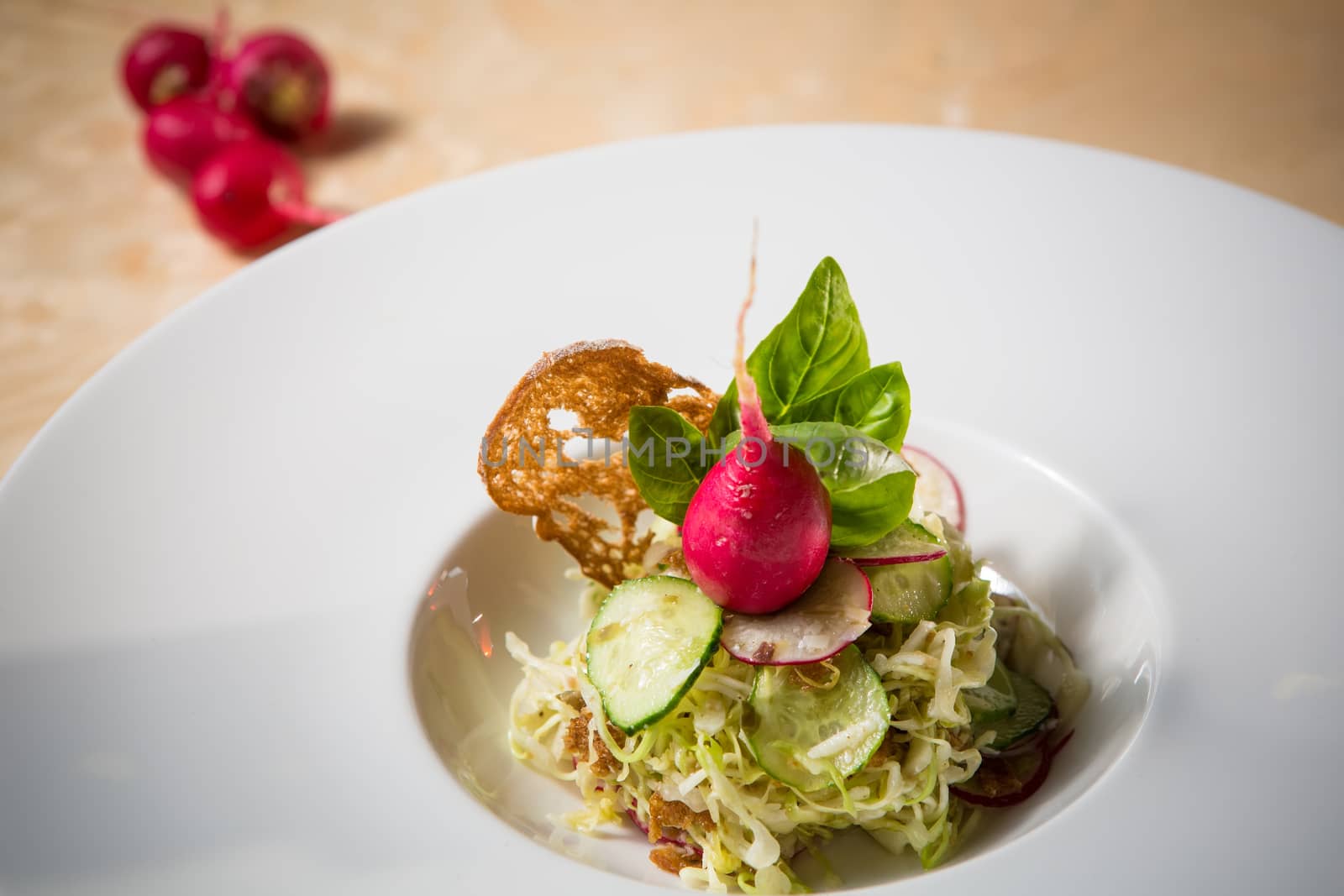 Salad from cabbage, herbs, cucumber, onion and radish in bowl on green wooden background. Coleslaw. Selective focus.