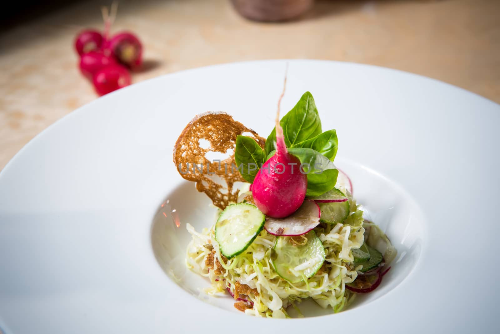 Salad from cabbage, herbs, cucumber, onion and radish in bowl on green wooden background. Coleslaw. Selective focus.