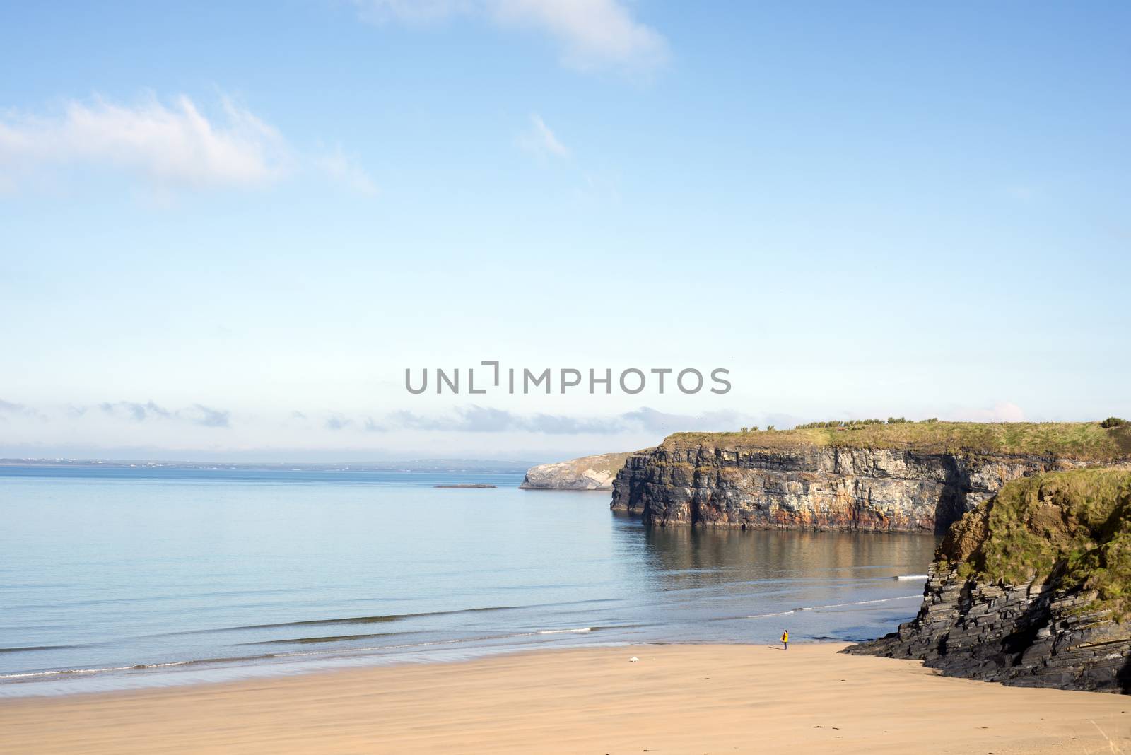 woman walking a dog as soft waves break on the beach cliffs at ballybunion