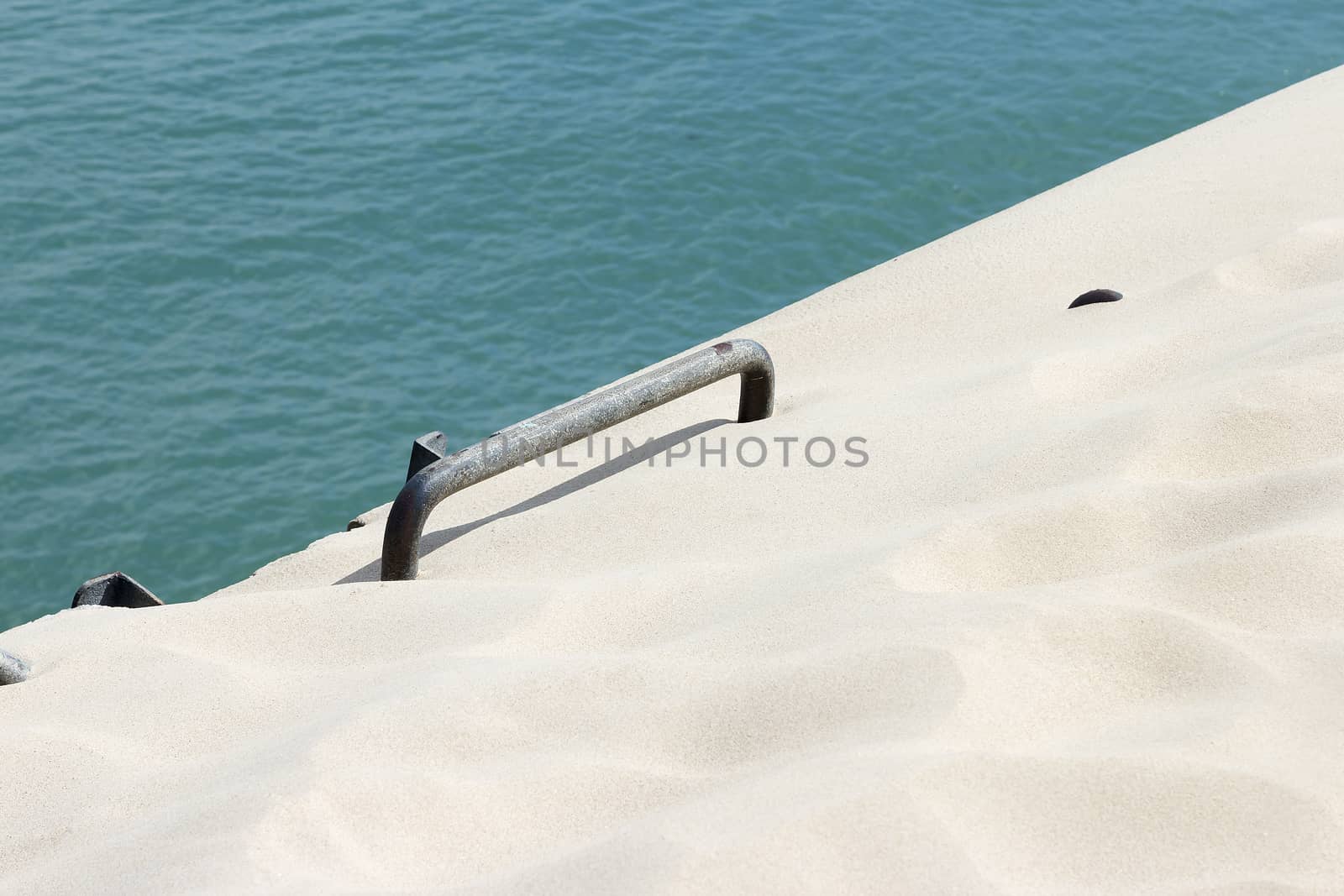 A ladder hidden in some sand in front of the water of the ocean