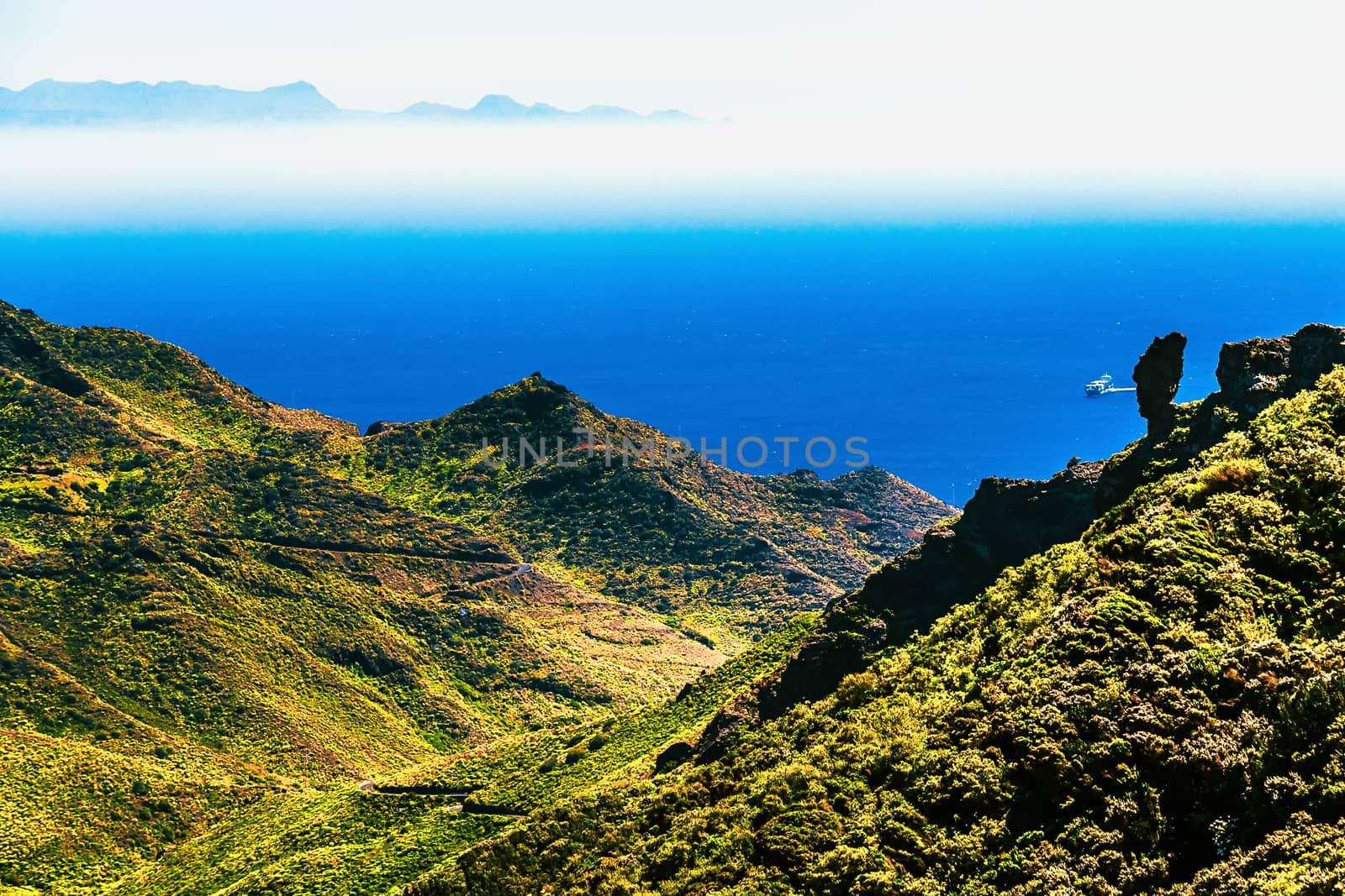 Coast or shore of Atlantic ocean with green mountain or rock with skyline and island in fog at background in Tenerife Canary island, Spain at spring or summer