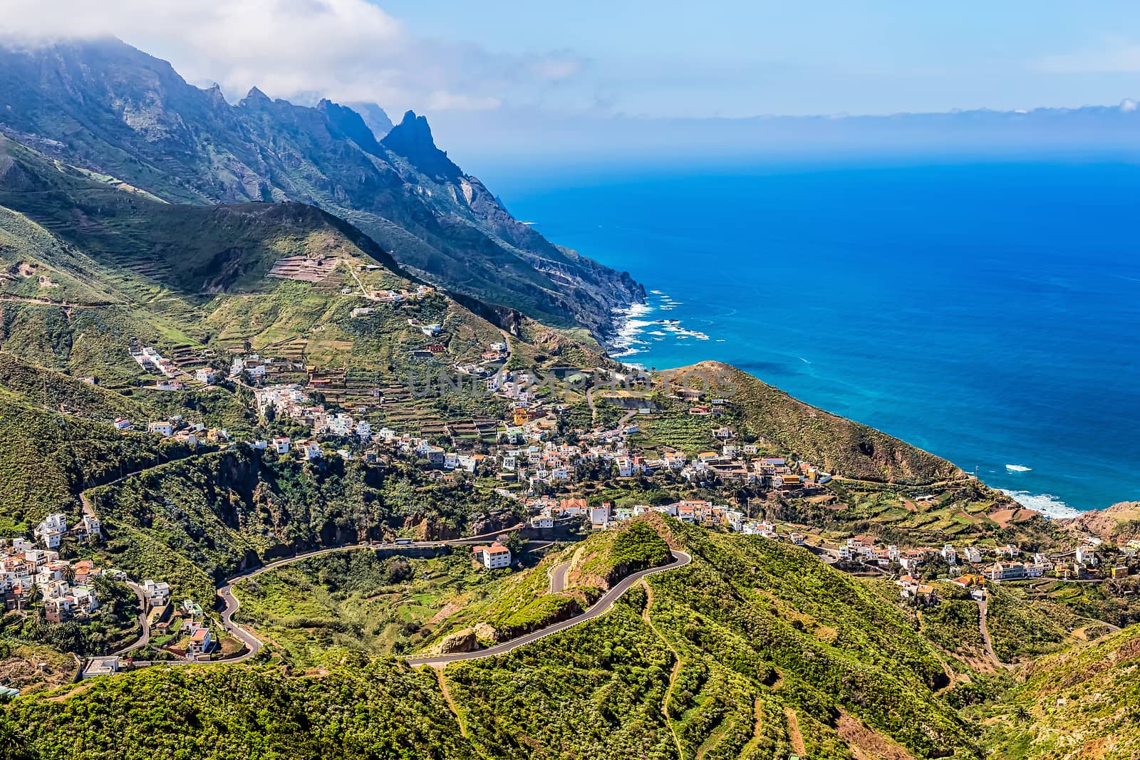 City or village buildings and winding or serpantine road in green mountain or rock valley and clouds with skyline landscape near shore of Atlantic ocean in Tenerife Canary island, Spain