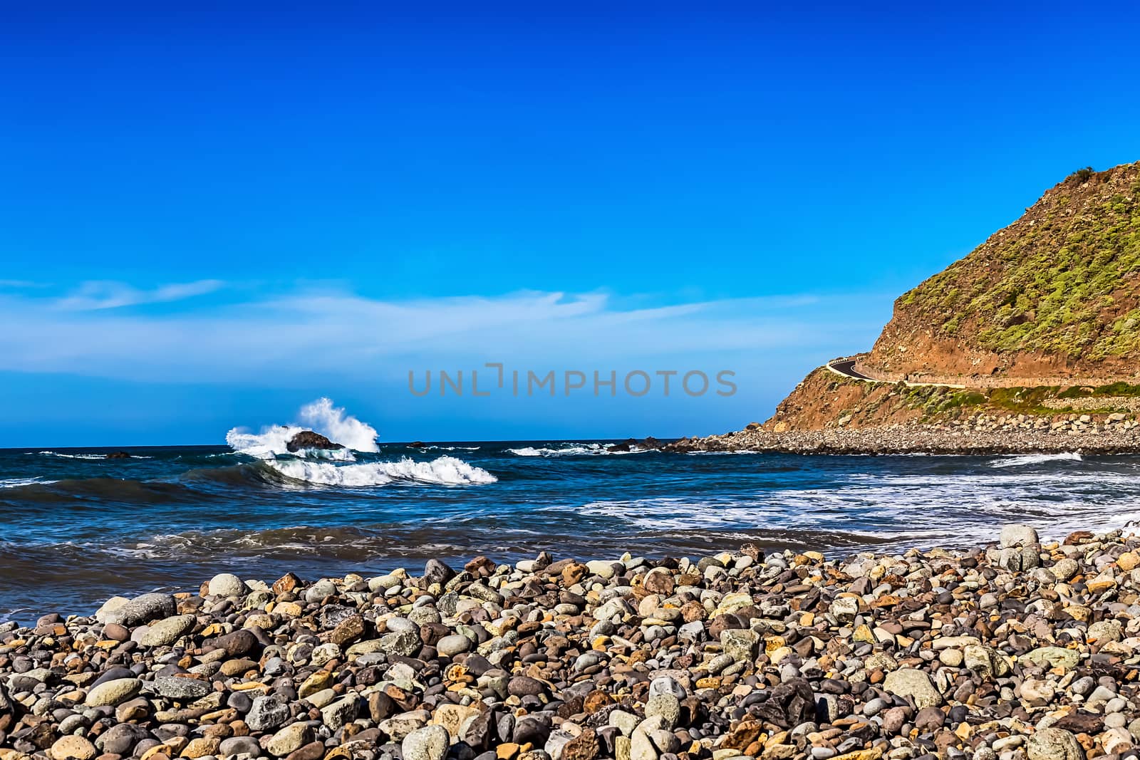 Wild stone beach and mountain on coast or shore of the Atlantic ocean with waves and sky with clouds and skyline or horizon in Tenerife Canary island, Spain at spring or summer