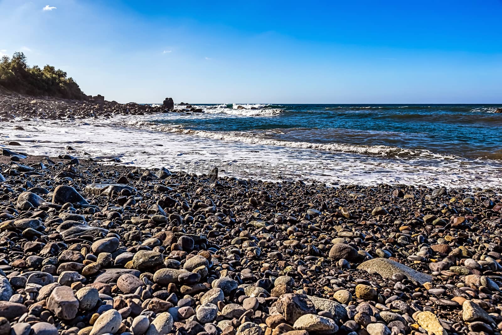 Wild stone beach on shore of the Atlantic ocean with waves and sky with clouds and skyline or horizon in Tenerife Canary island, Spain at spring or summer