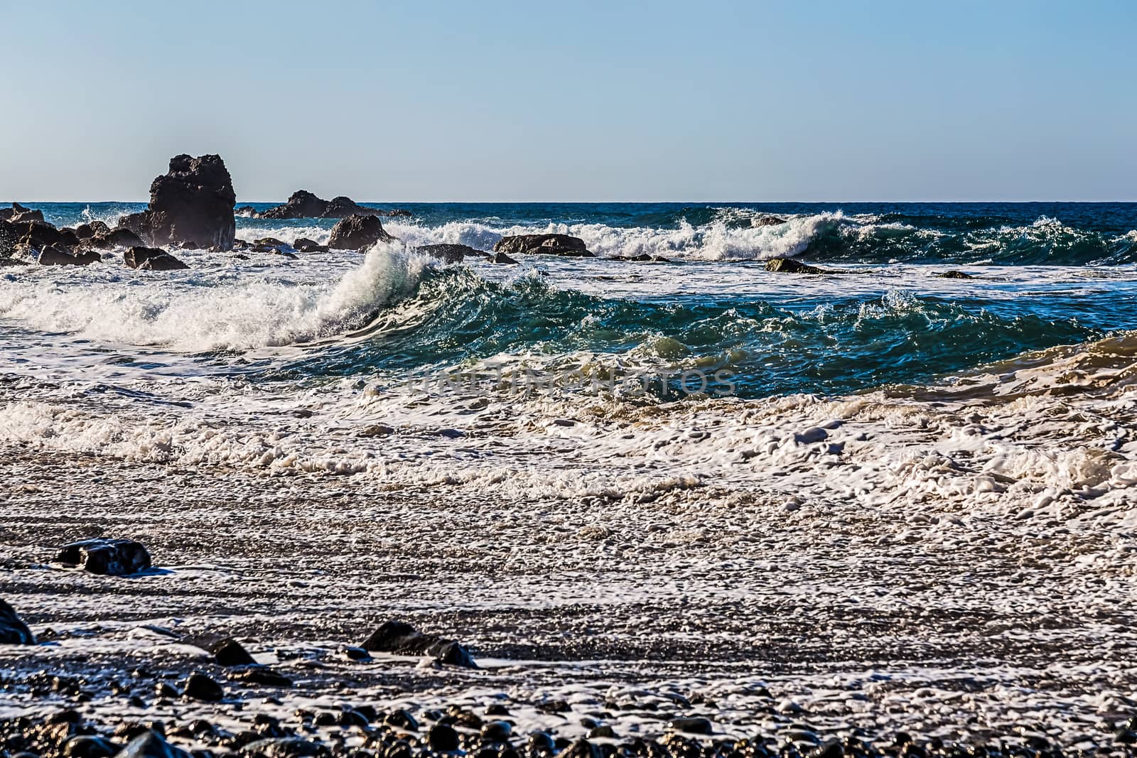 Waves and foam on wild stone beach on coast of the Atlantic ocean with sky and rock on skyline or horizon in Tenerife Canary island, Spain at spring or summer