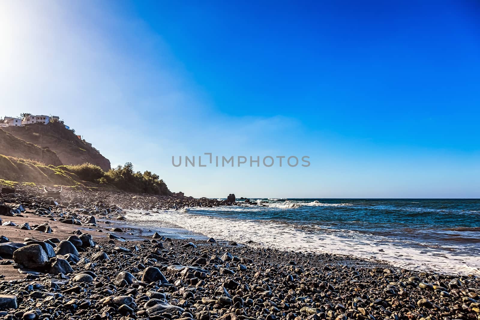 Wild stone beach on coast or shore of the Atlantic ocean with waves and blue sky and skyline or horizon in Tenerife Canary island, Spain