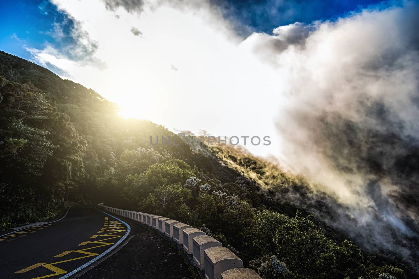 Asphalt road in mountains or rocks and sky with sun and sunlight and clouds over peak in Tenerife Canary island, Spain at sunset
