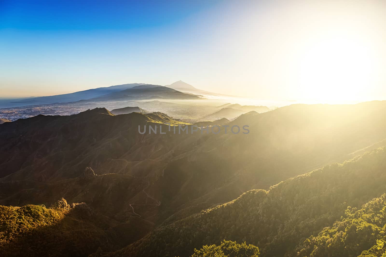 Sun with sunlight over mountains on blue sky with fog or haze and Teide volcano on background at evening sunset in Tenerife Canary island, Spain at spring or summer