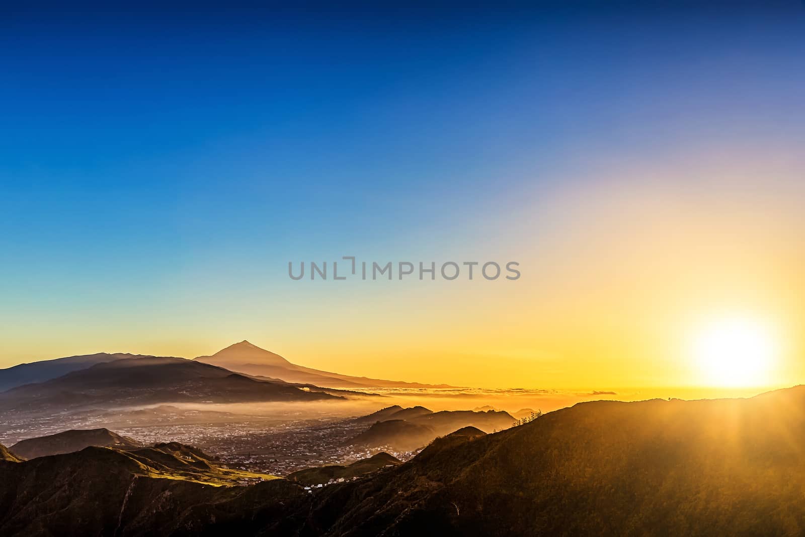 Sun with sunlight over mountains on blue sky with haze and Teide volcano on background at evening sunset in Tenerife Canary island, Spain at spring or summer