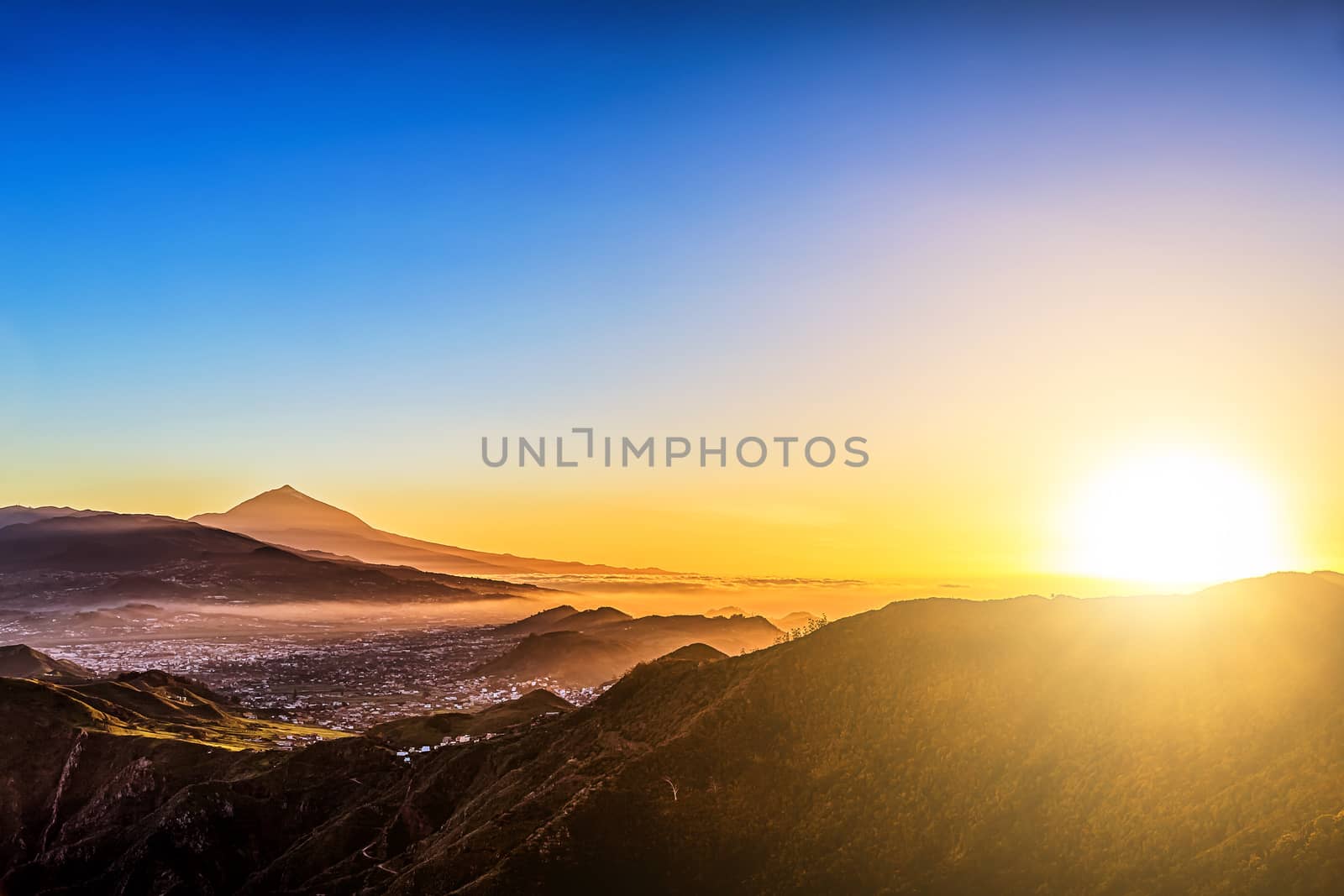 Sun with sunlight over mountains on blue sky with haze and Teide volcano on background at evening sunset in Tenerife Canary island, Spain