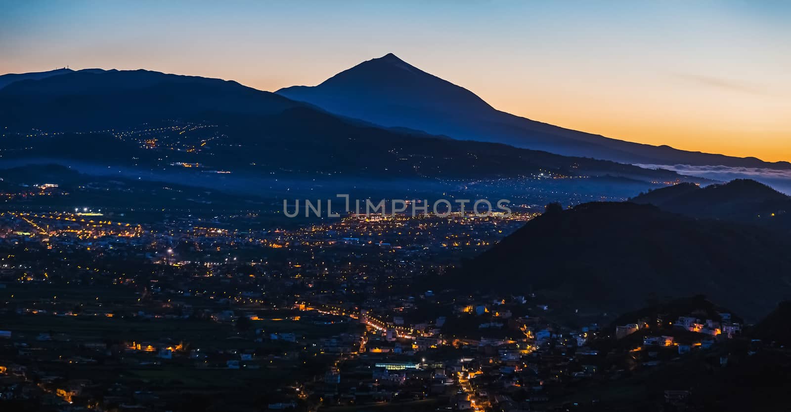City with illumination after sunset at evening in mountains with blue sky and Teide volcano on background panorama in Tenerife Canary island, Spain at spring or summer