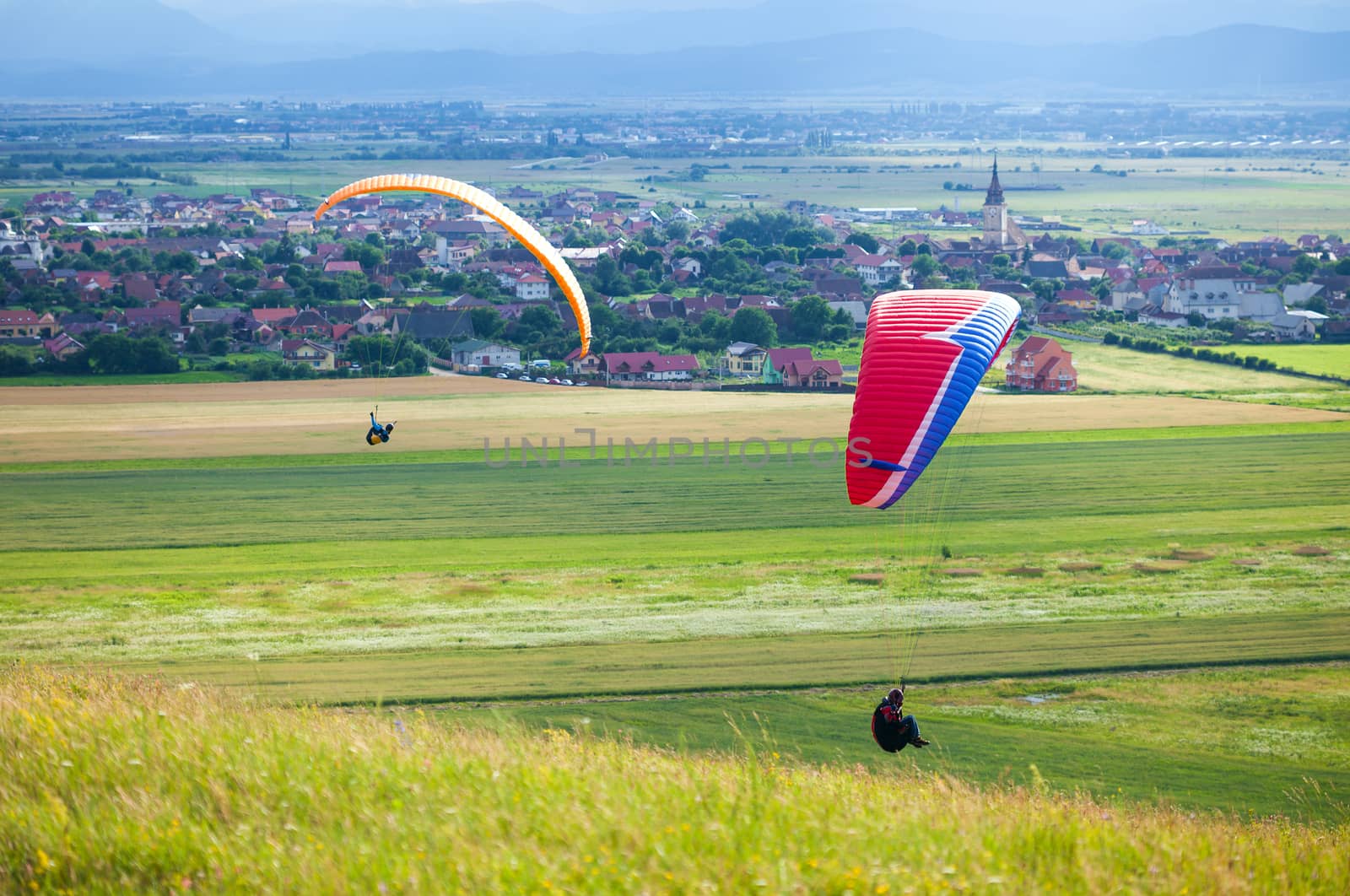 Paragliders flying over green fields with typical romanian village on background