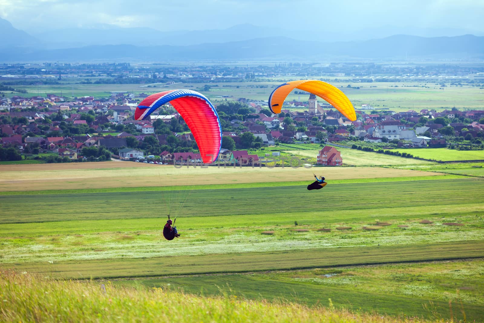 Paragliders flying over green fields with typical romanian village on background