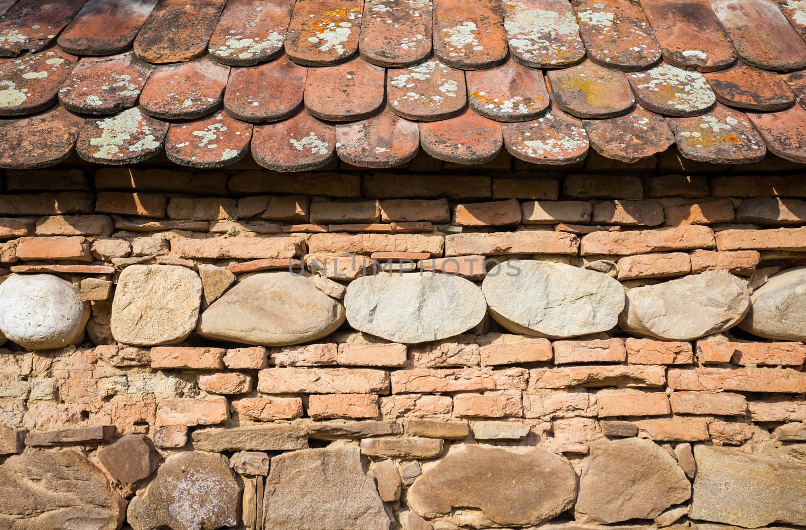 Rustic wall with layers of different comstruction materials - sandstones, bricks, river stones and roof tiles