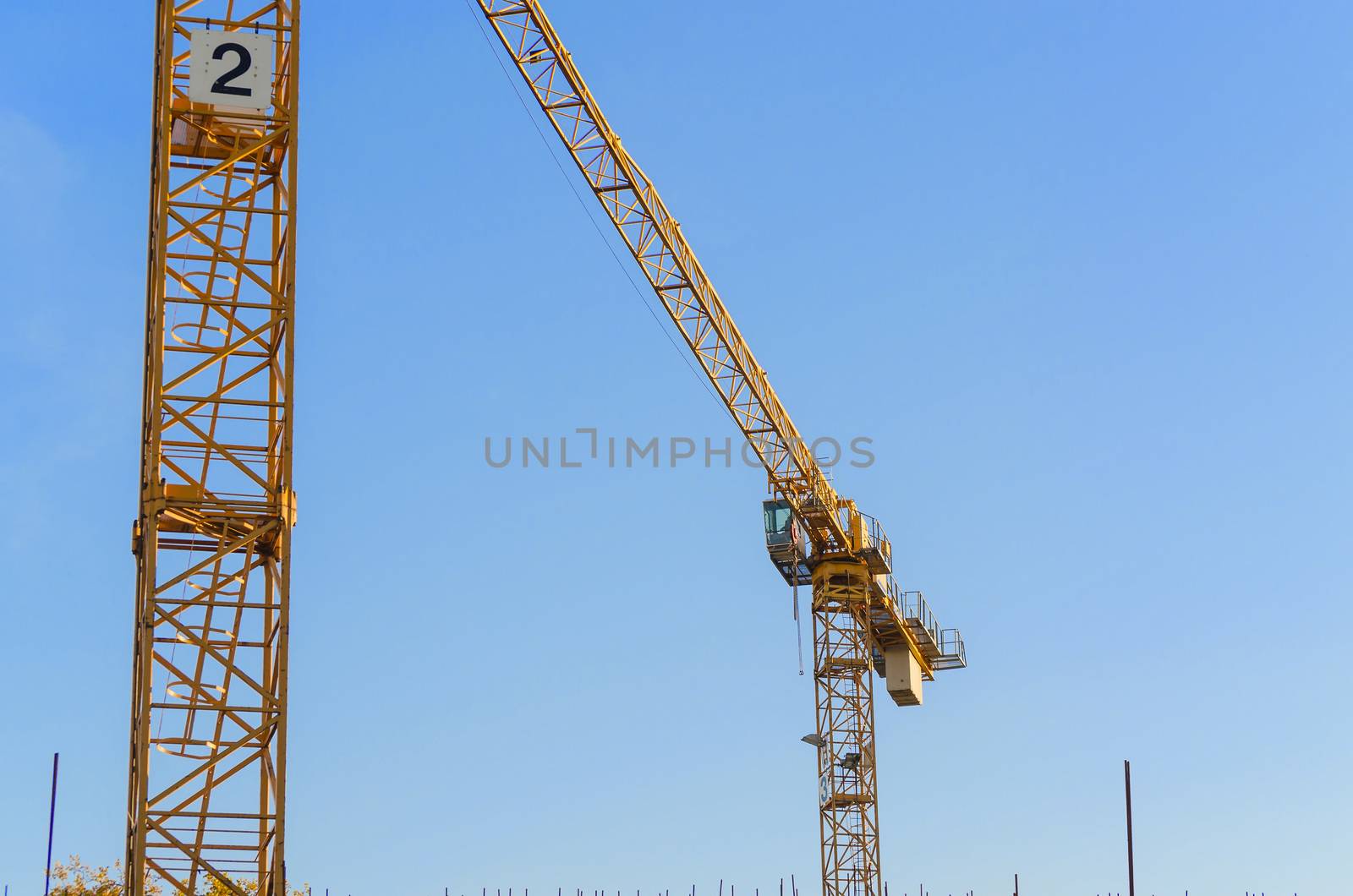 Two Construction cranes on a construction site against a blue sky.