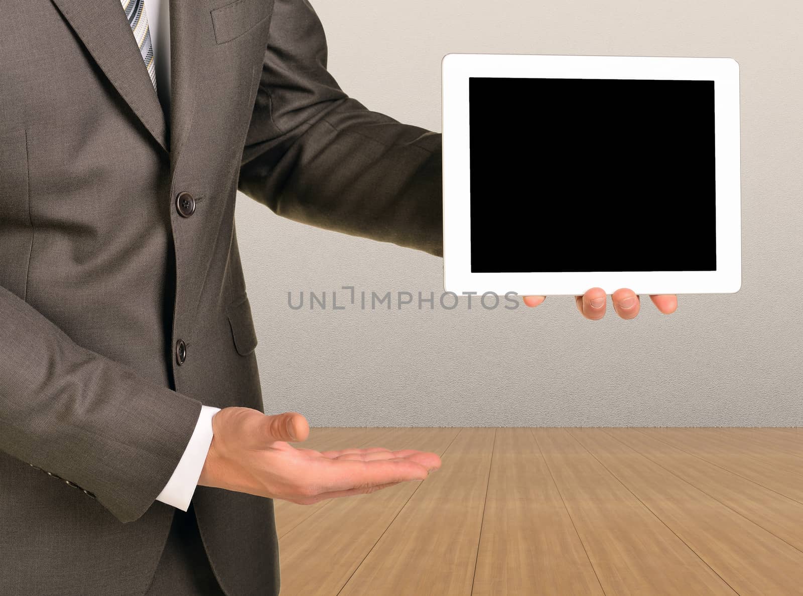 Your concept on the tablet. Man holding tablet. Wooden floor and gray wall in background