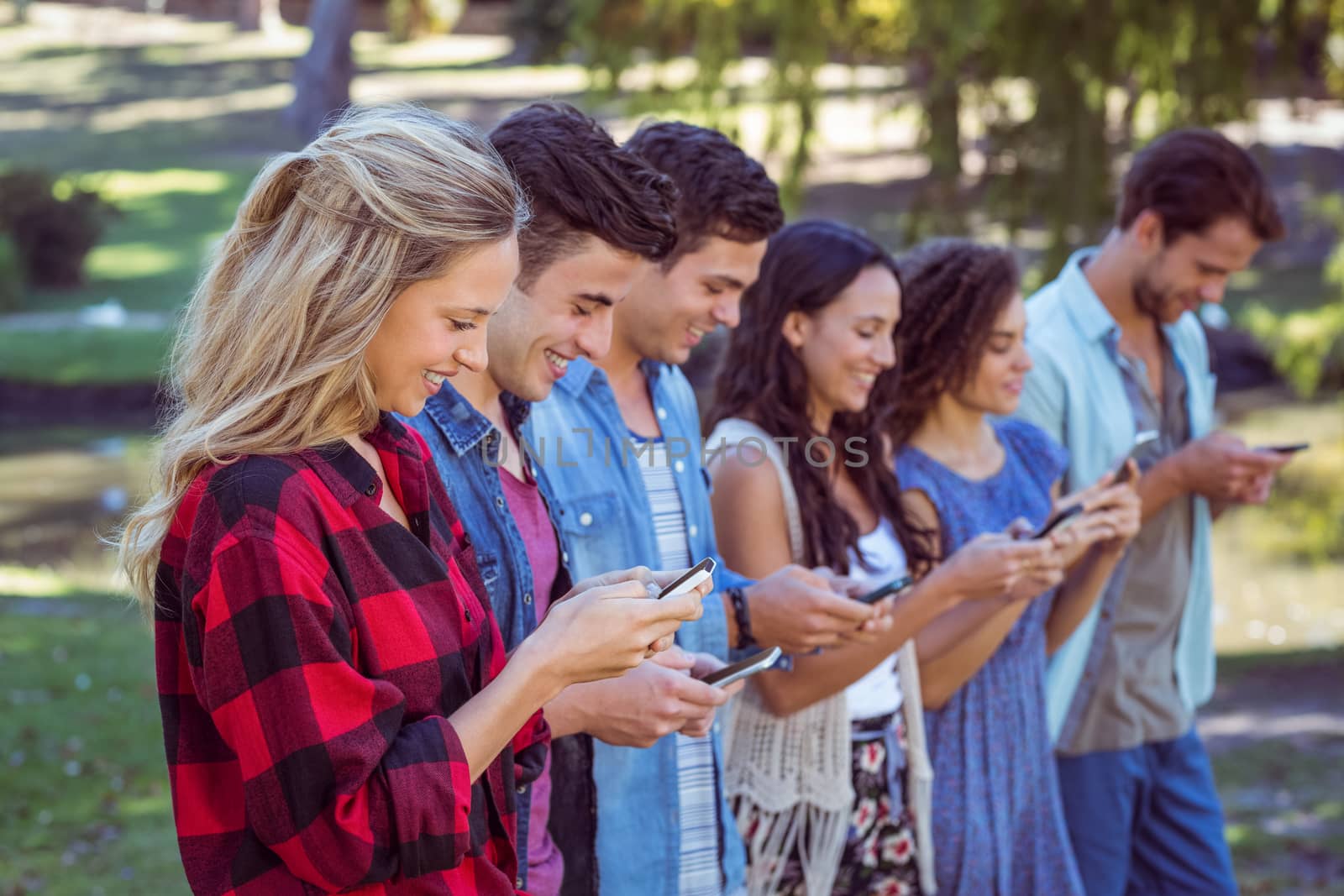 Happy friends in the park using their phones on a sunny day