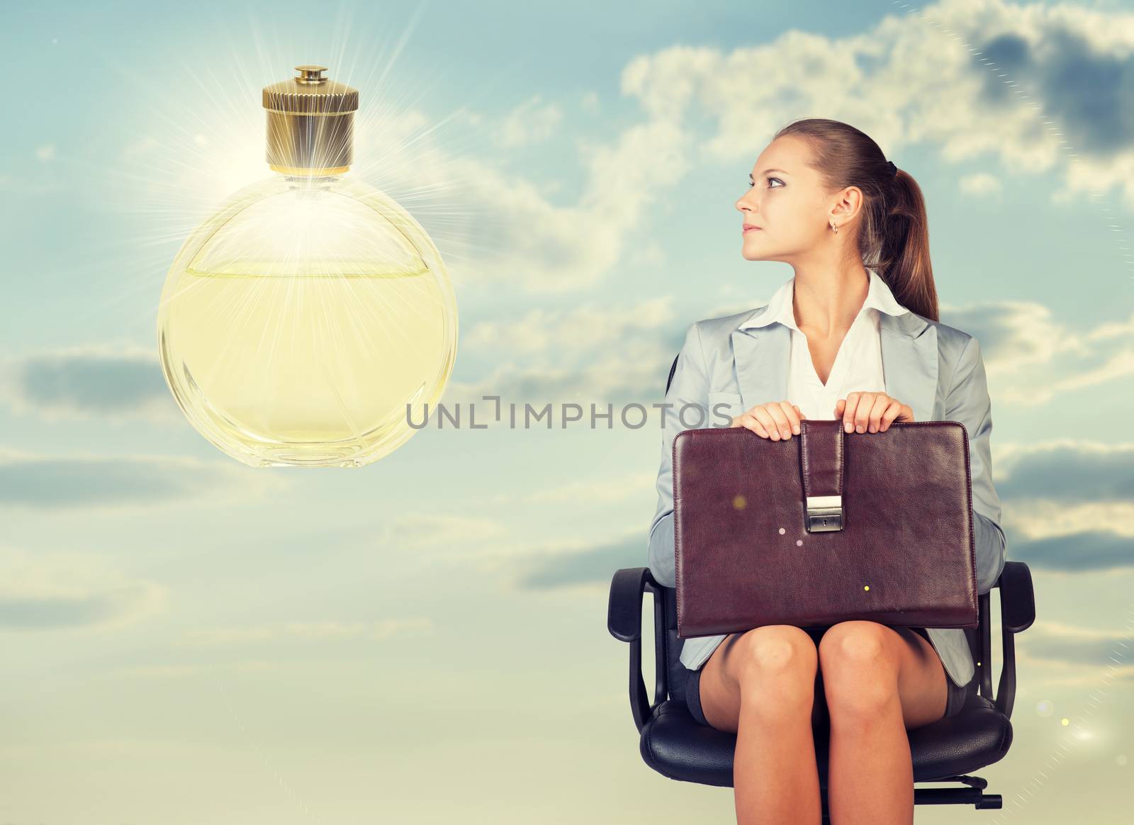 Business woman in skirt, blouse and jacket, sitting on chair, holding briefcase imagines perfume. Against background of sky, clouds by cherezoff