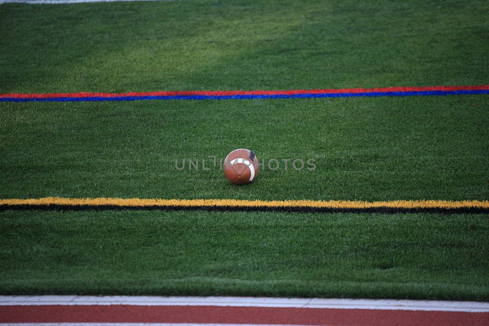 A football game ball rests on a turf grass field in between sideline markers.