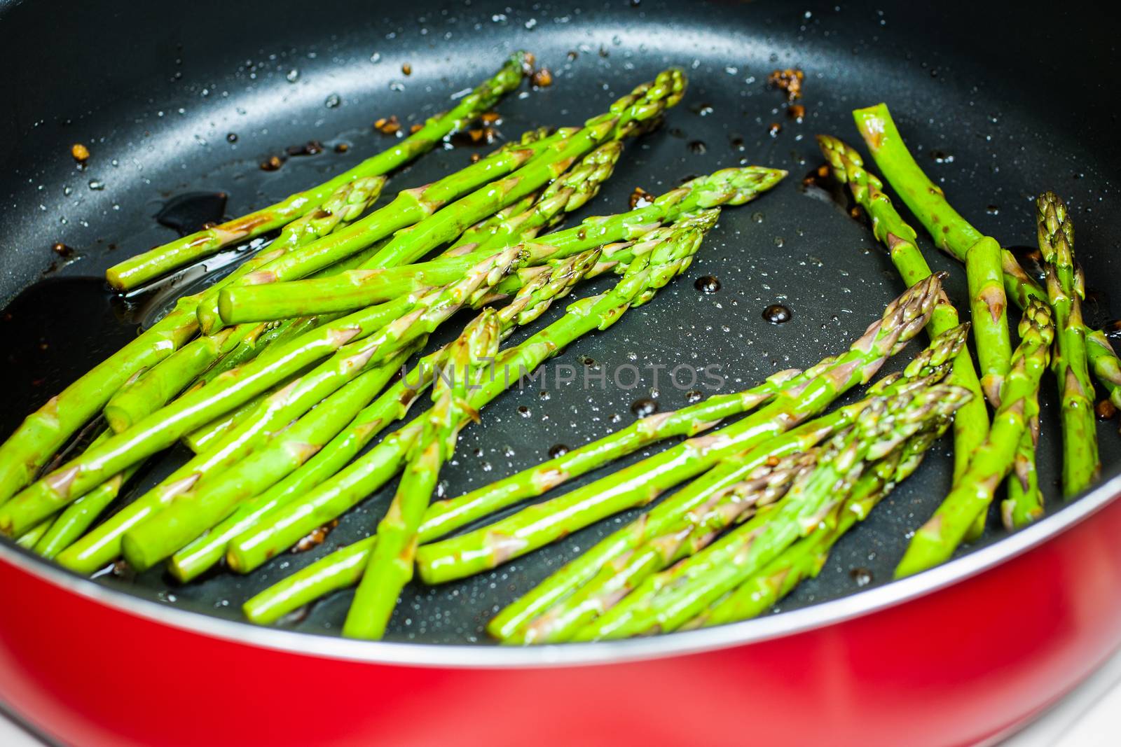 Fresh asparagus cooking in a pan with soy, ginger, and garlic.