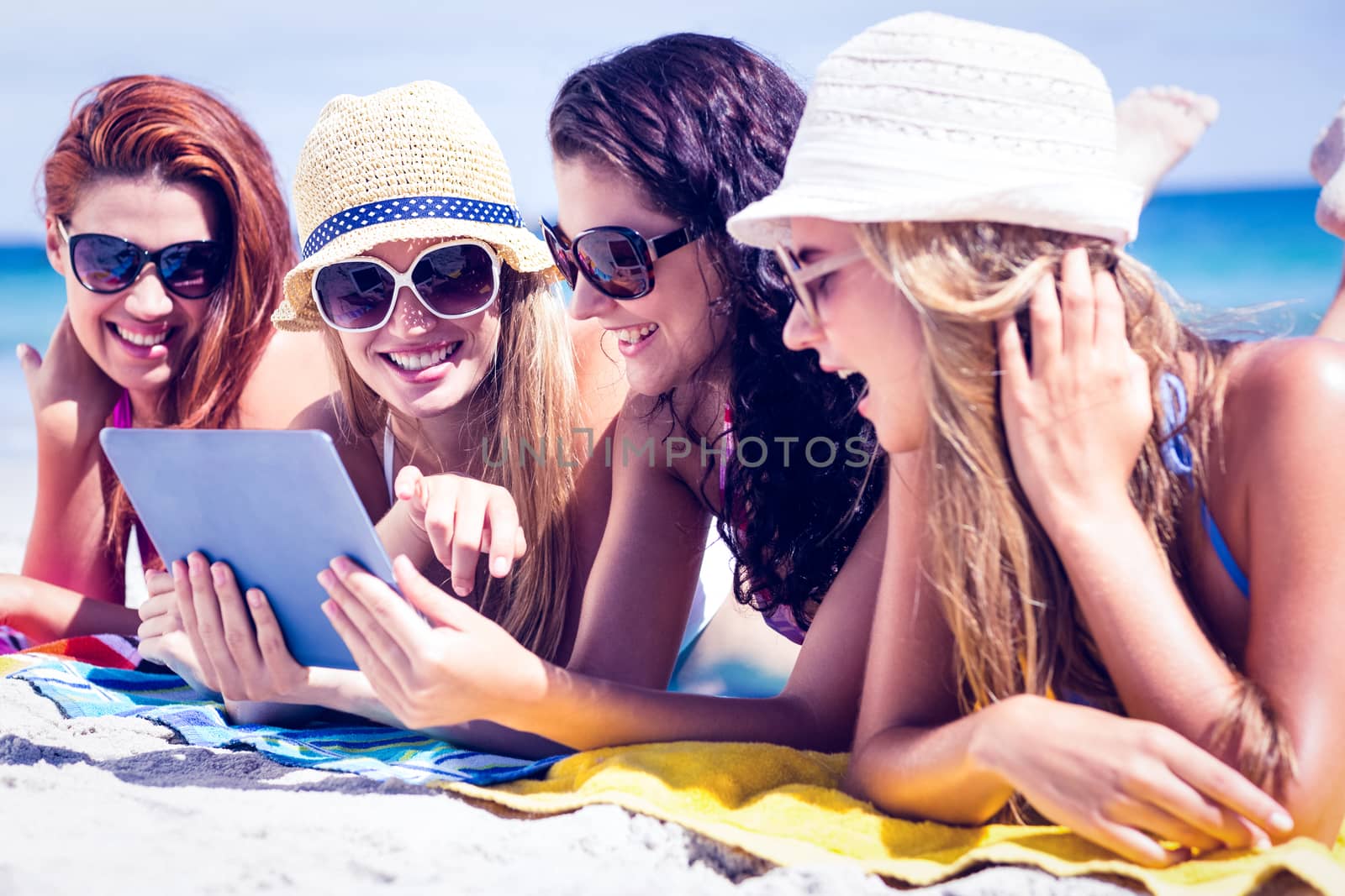 Happy friends wearing sunglasses and using tablet at the beach