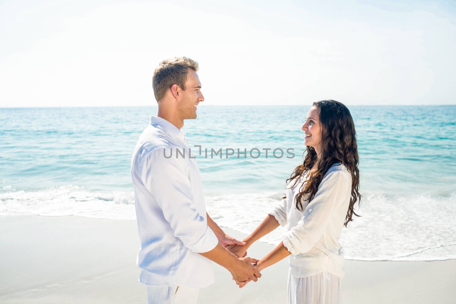 Romantic casual young couple holding hands and standing at the beach