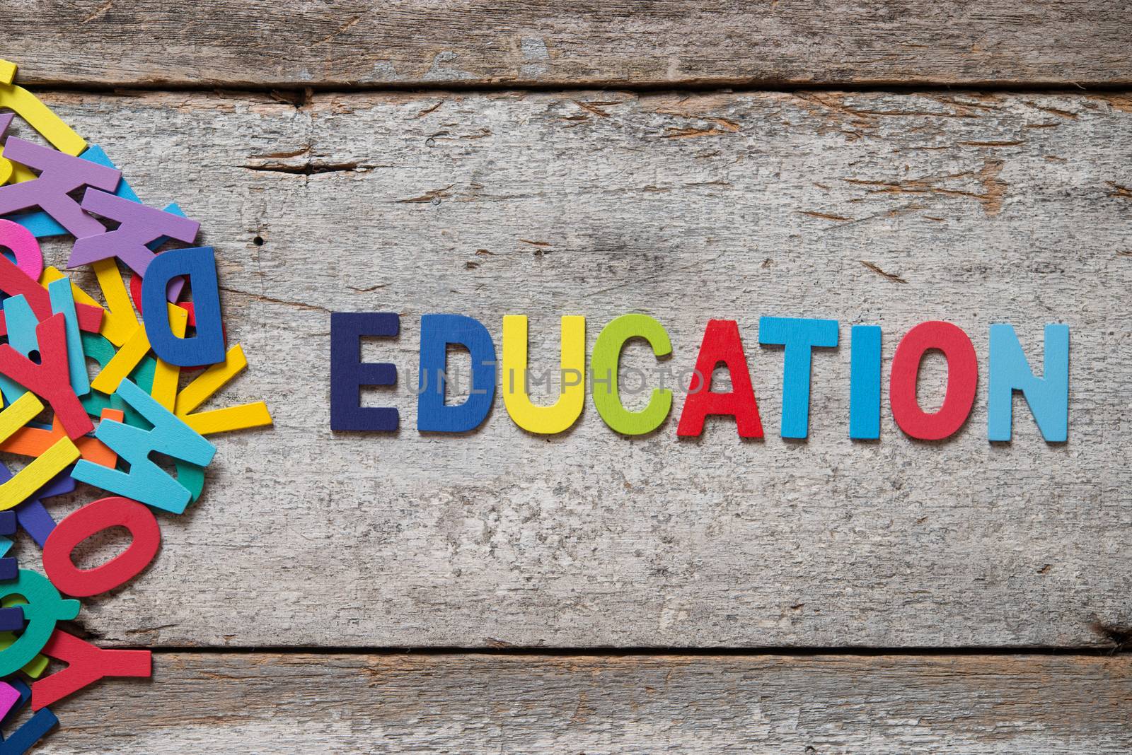 The colorful words "EDUCATION" made with wooden letters next to a pile of other letters over old wooden board.
