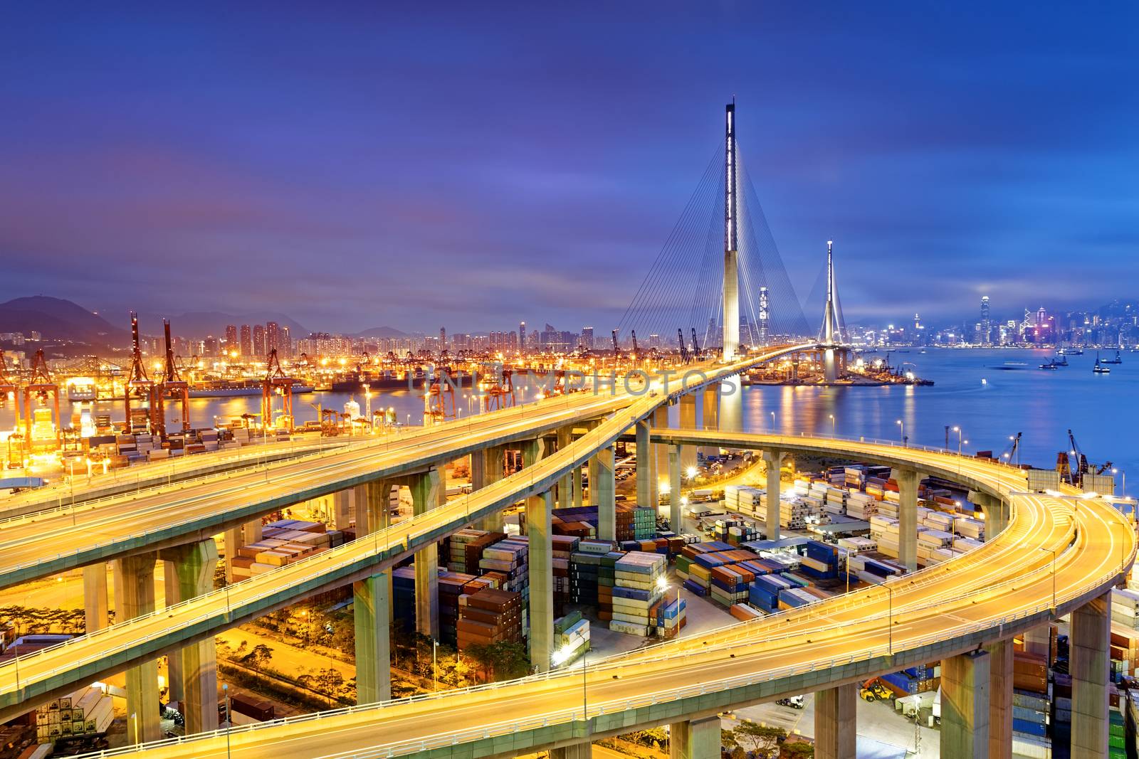 Container Cargo freight ship with working crane bridge in shipyard under Stonecutters highway bridge at sunset for Logistic Import Export, Hong kong