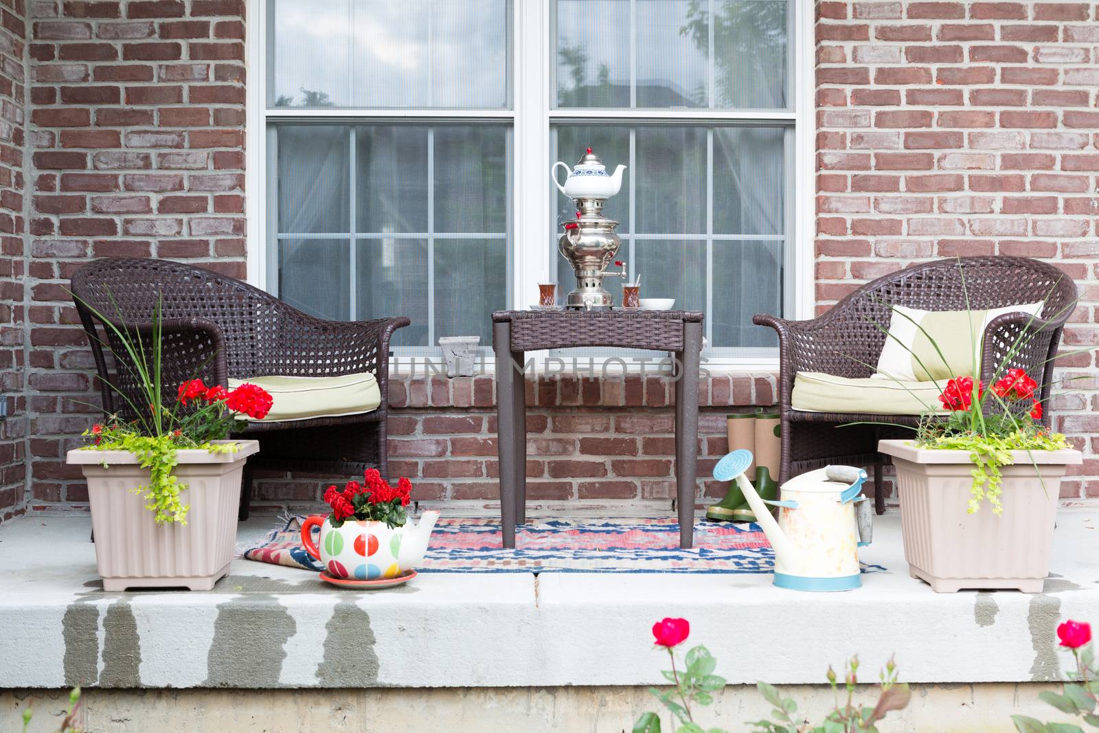 Wicker furniture on the patio with a samovar and tea cups ready for a relaxing tea break in the spring sunshine with pretty flowering potted plants