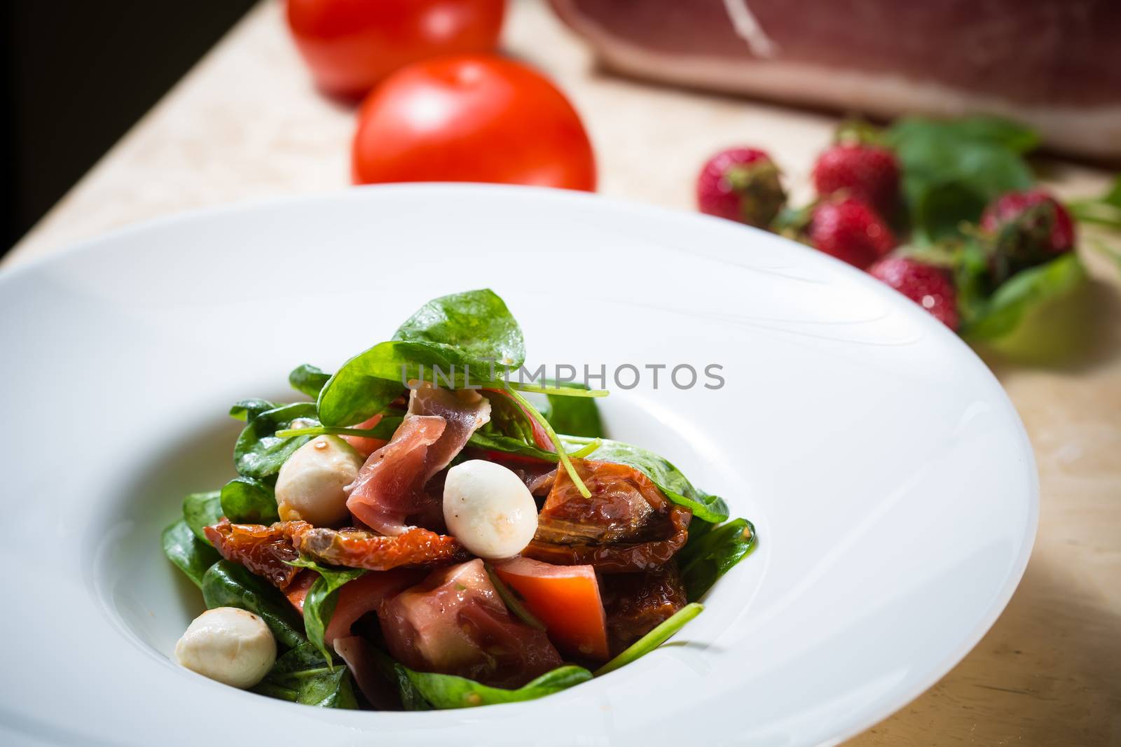 Salad with strawberry, prosciutto, herbs, cottage cheese and blackberry balsamic vinegar. Shallow dof.