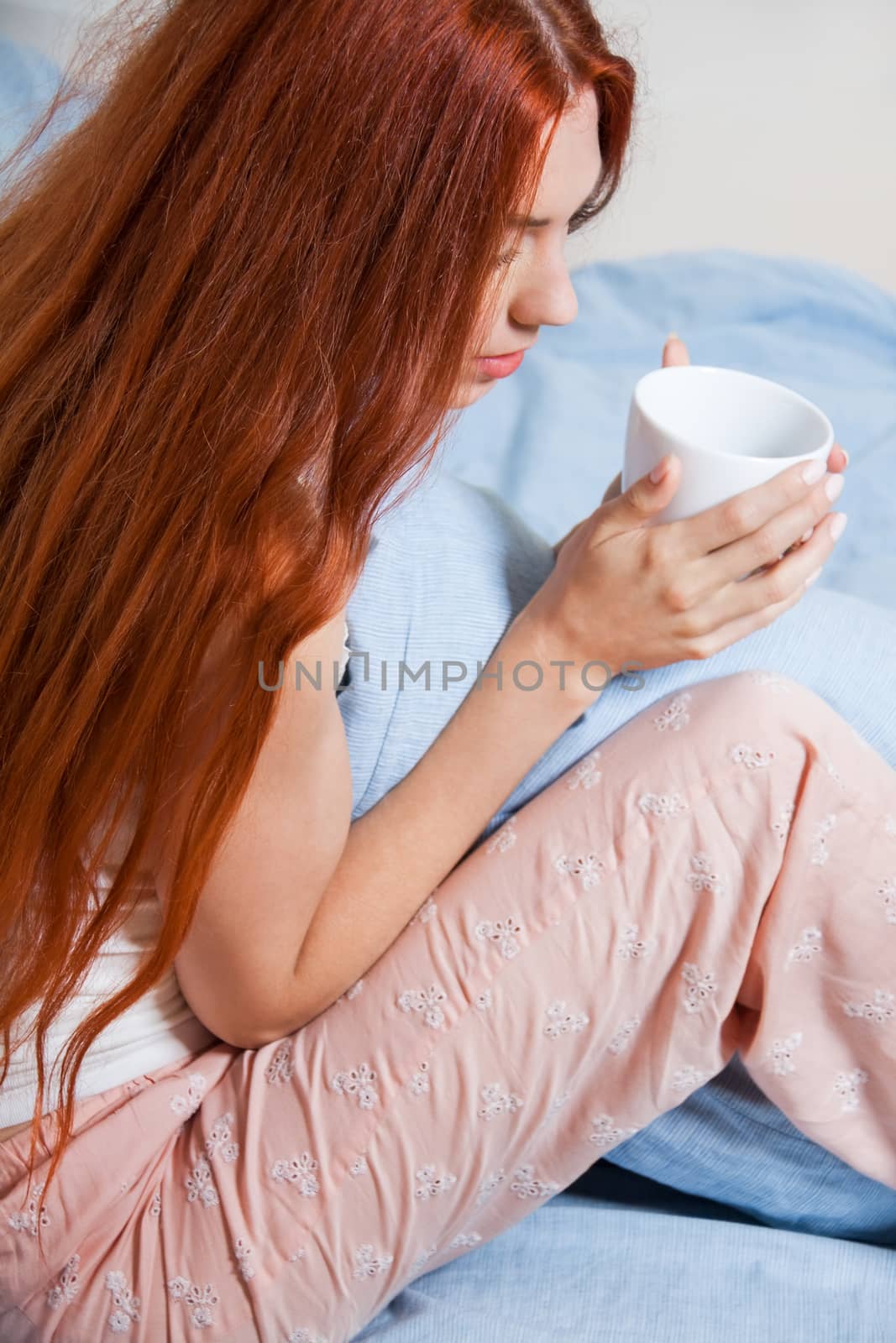 Close up Pensive Blond Woman Holding a White Cup of Coffee While Sitting on her Bed After Waking Up.