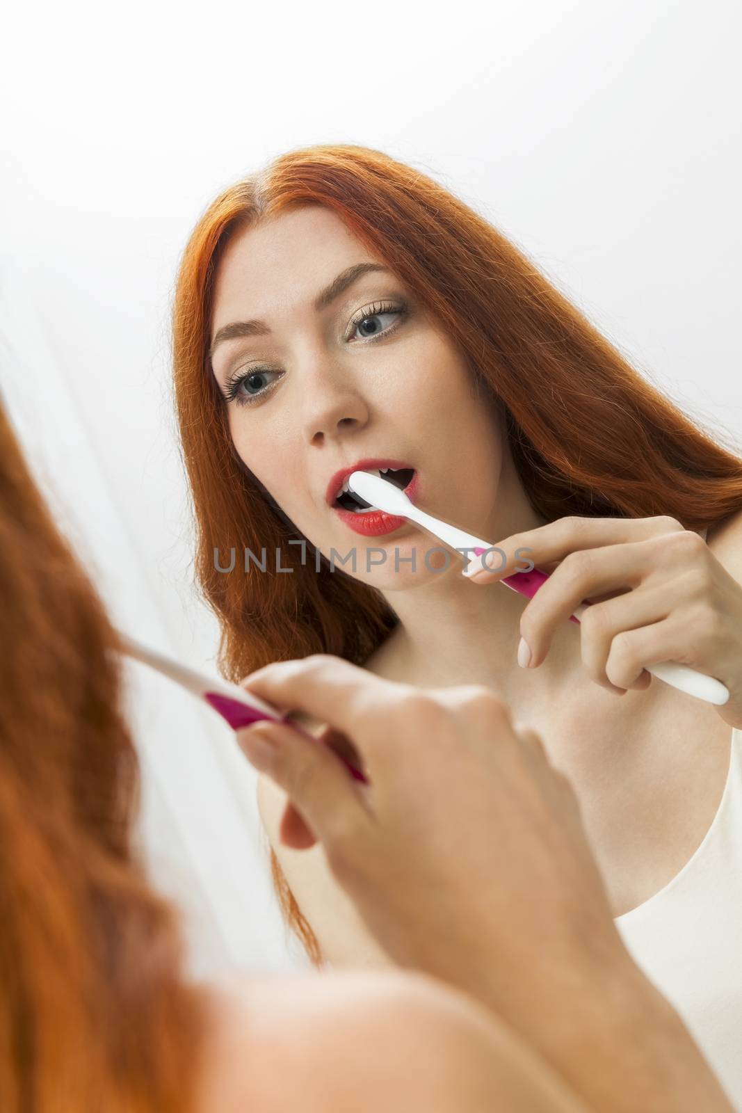 Close up Pretty Young Woman with Long Blond Hair Brushing her Teeth in Front a Mirror