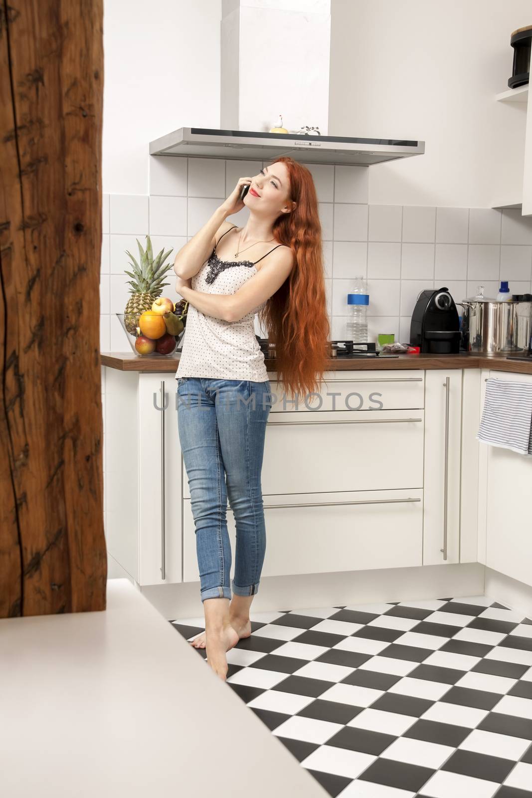 Portrait of a Happy Young Woman with Long Wavy Blond Hair Talking Through Phone at the Home Kitchen Area