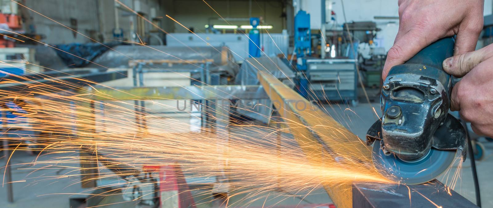 Electric wheel grinding on steel structure in factory.