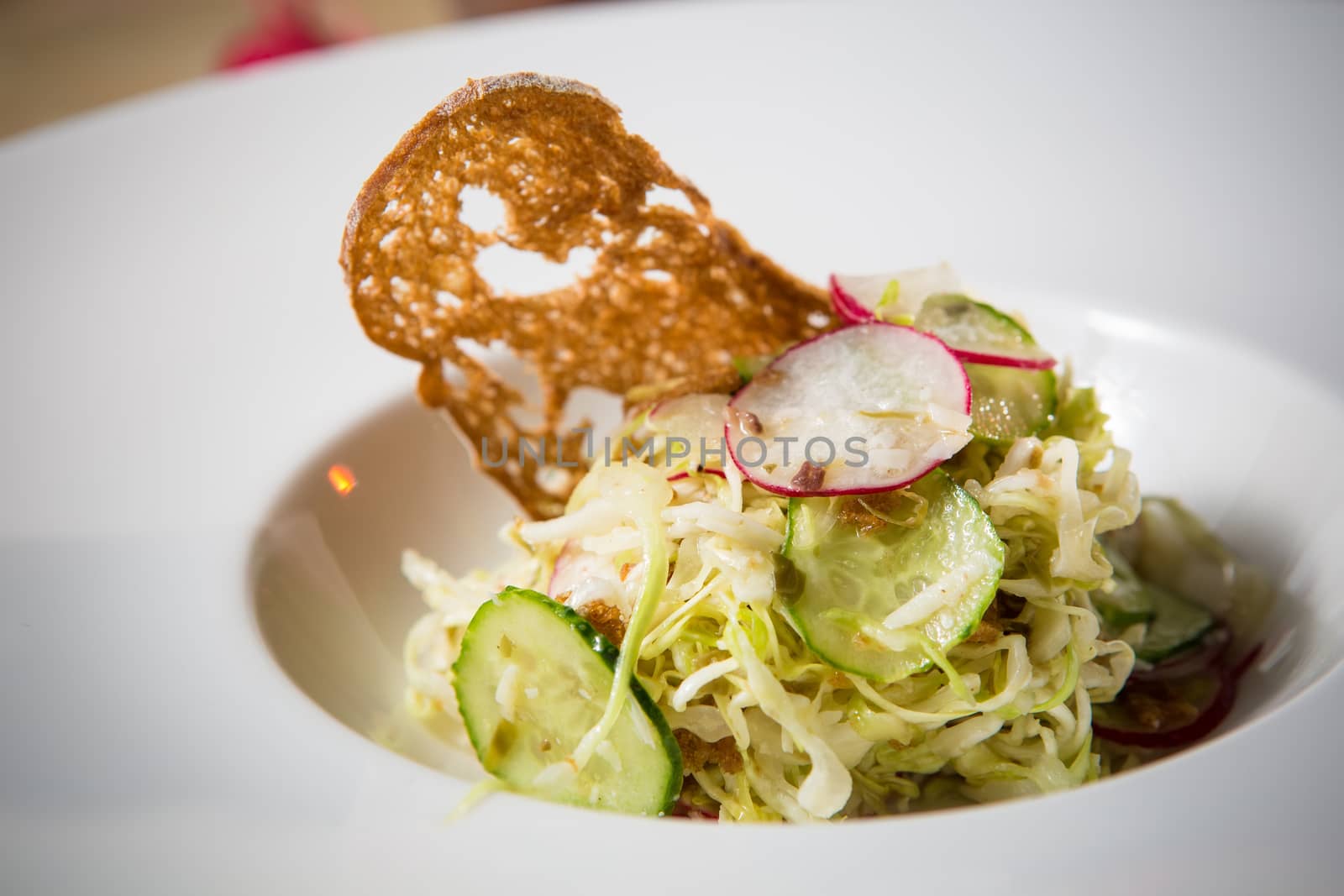 Salad from cabbage, herbs, cucumber, onion and radish in bowl on green wooden background. Coleslaw. Selective focus.
