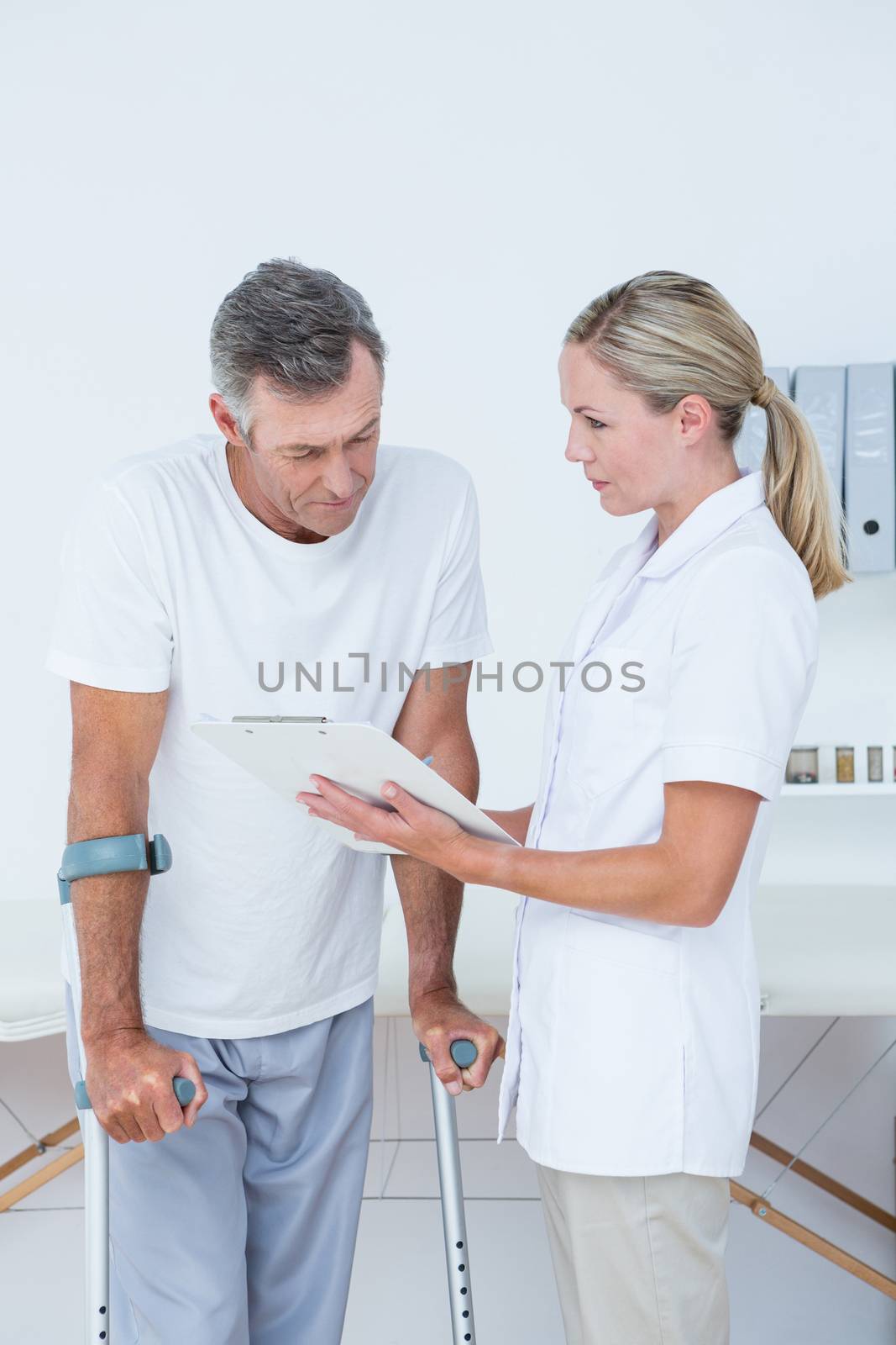 Doctor showing clipboard to her patient with crutch in medical office