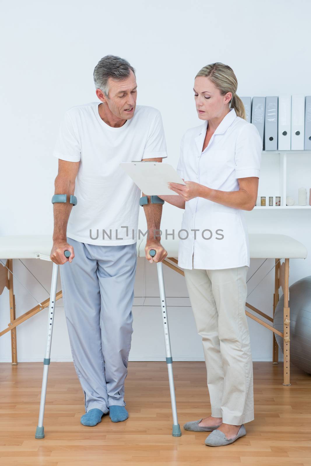 Doctor showing clipboard to her patient with crutch in medical office