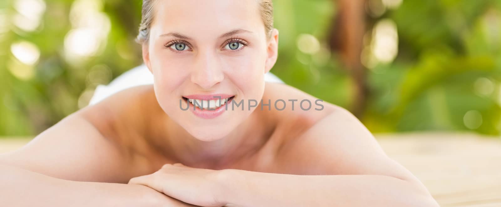 Peaceful blonde lying on towel smiling at camera at the health spa