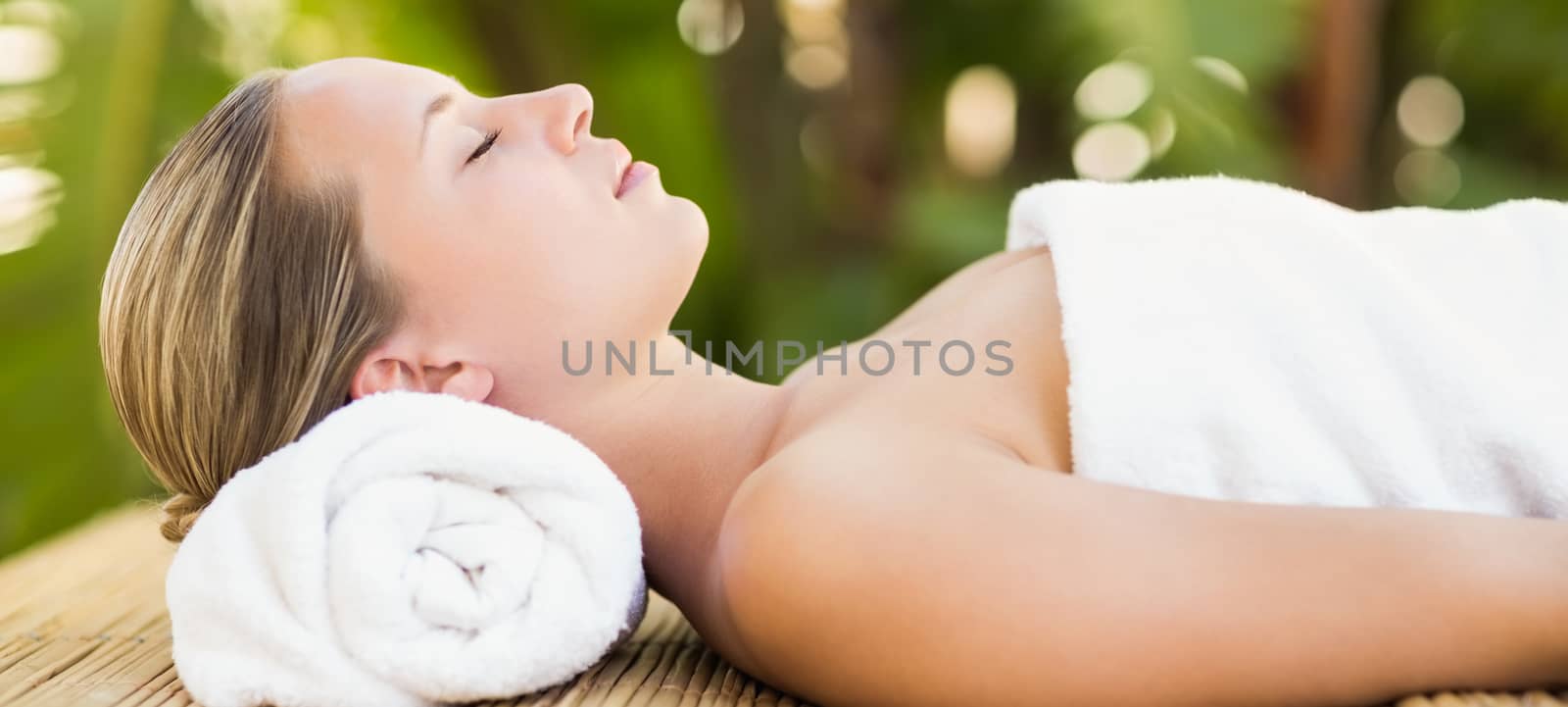 Peaceful blonde lying on bamboo mat with flowers at the health spa