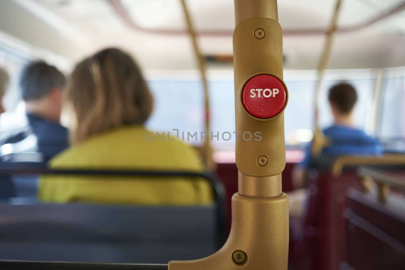 Detail of red stop button inside double decker bus in London, UK, with passengers seated in the blurred background.