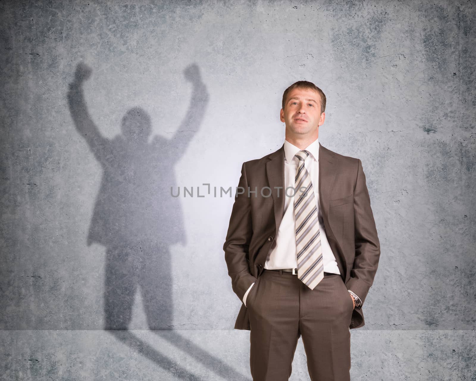 Businessman with shadow showing win on wall texture background, looking at camera