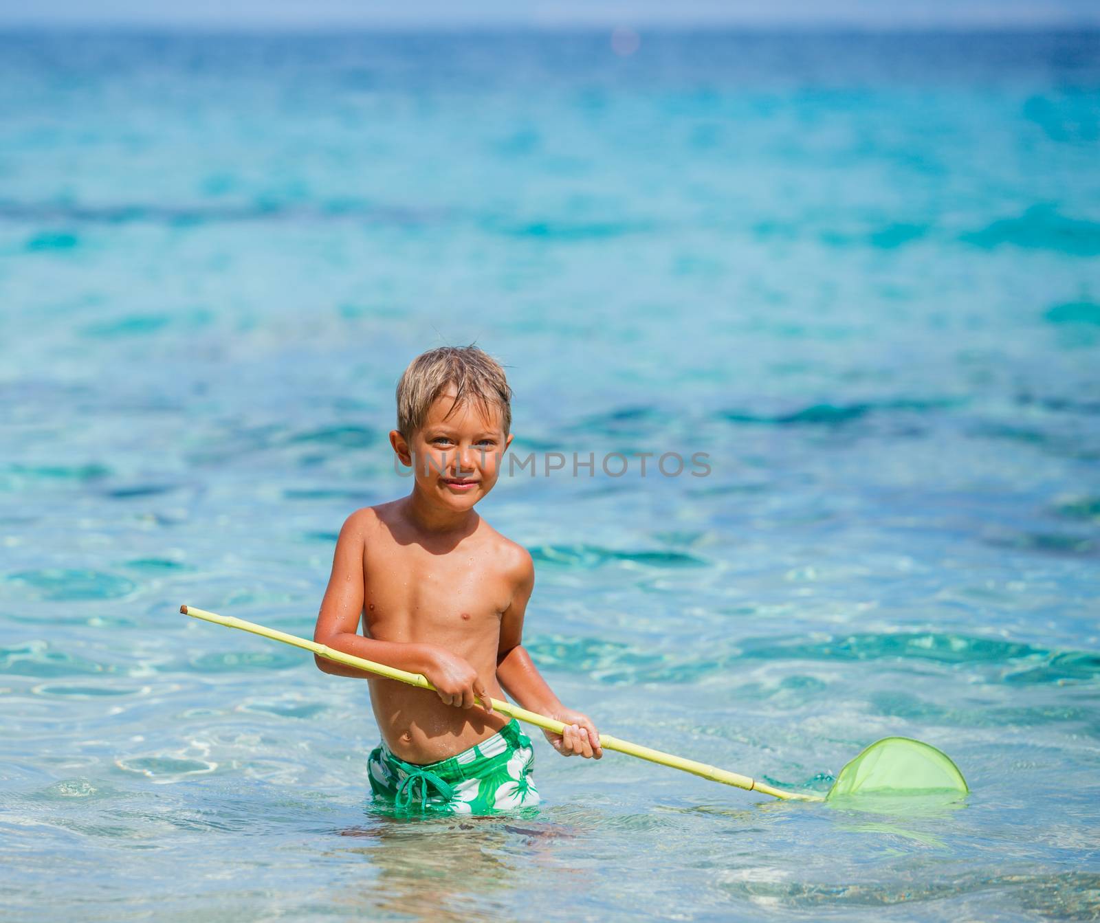 Cute boy playing with scoop-net and swimming in the transparent sea