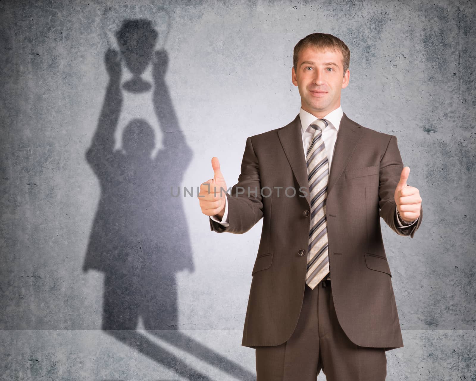 Businessman with shadow holding winner cup on wall texture background, looking at camera