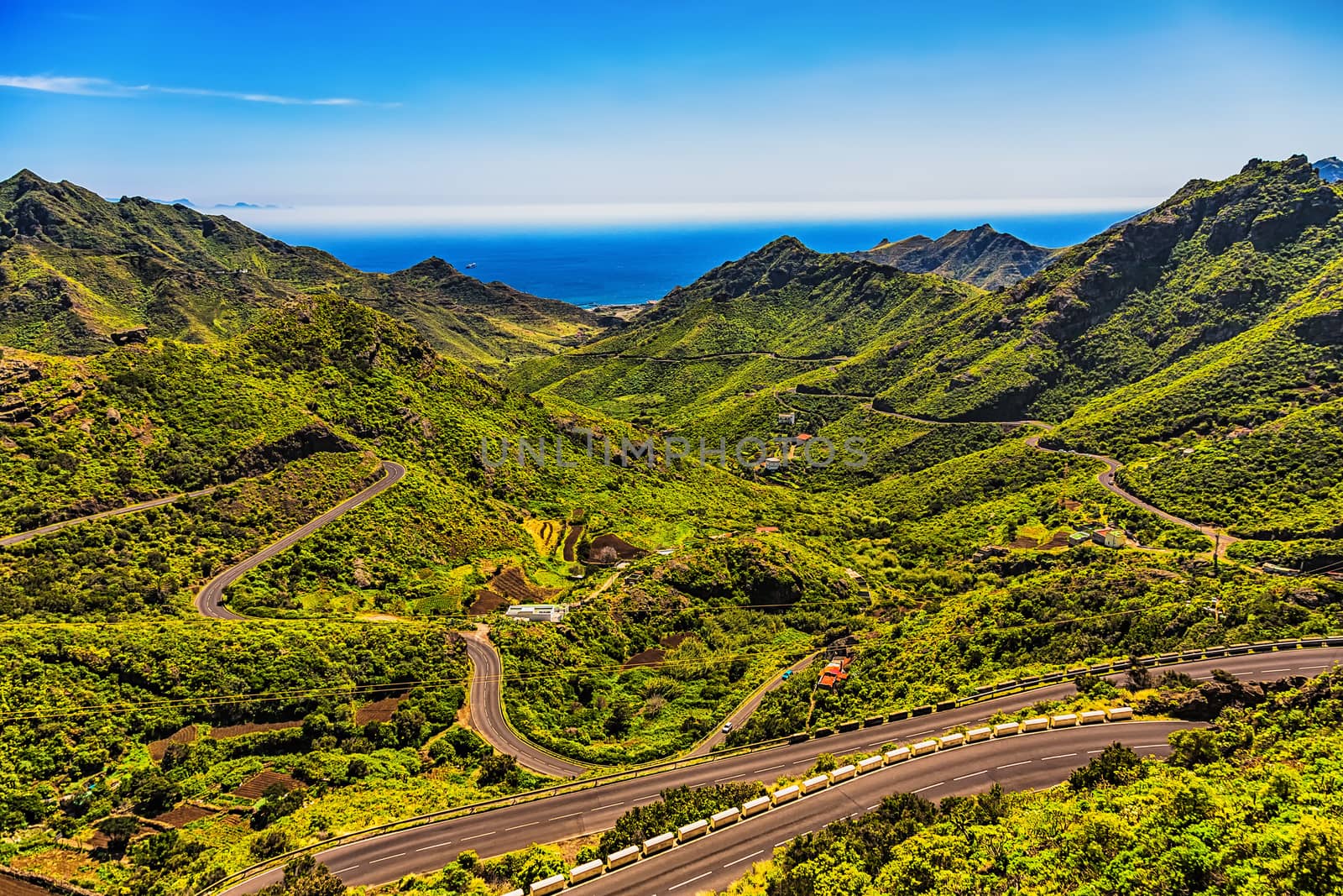 Green mountains or rocks valley with winding or serpantine road and sky with ocean on skyline landscape in Tenerife Canary island, Spain at summer