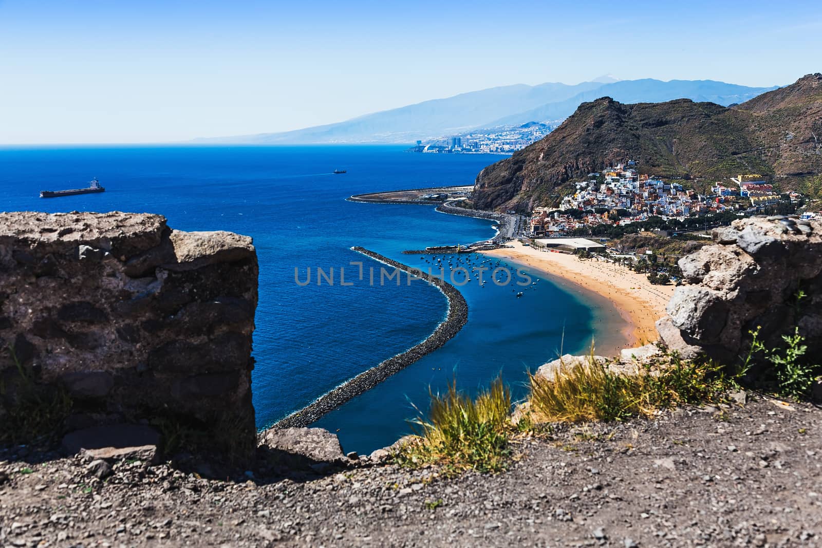 Aerial view through stones to beach or playa Las Teresitas in Santa Cruz city on coast or shore of the Atlantic ocean on Tenerife Canary island, Spain at spring or summer. Teide volcano at background