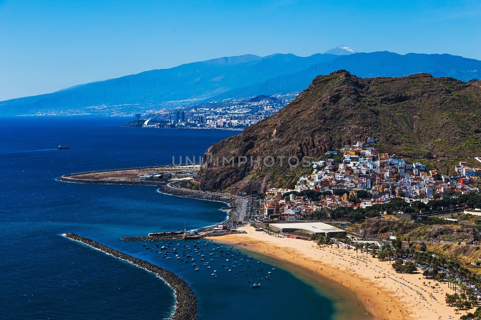 Aerial view from mountain to Santa Cruz city and beach or playa Las Teresitas on coast or shore of the Atlantic ocean on Tenerife Canary island, Spain at spring or summer. Teide volcano at background