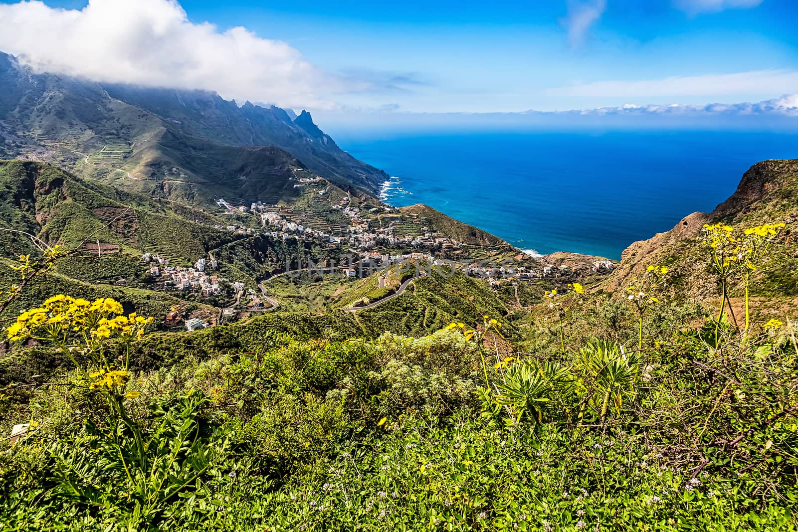 Small city or village and winding or serpantine road in green mountain or rock valley and clouds with horizon landscape near  shore of Atlantic ocean in Tenerife Canary island, Spain