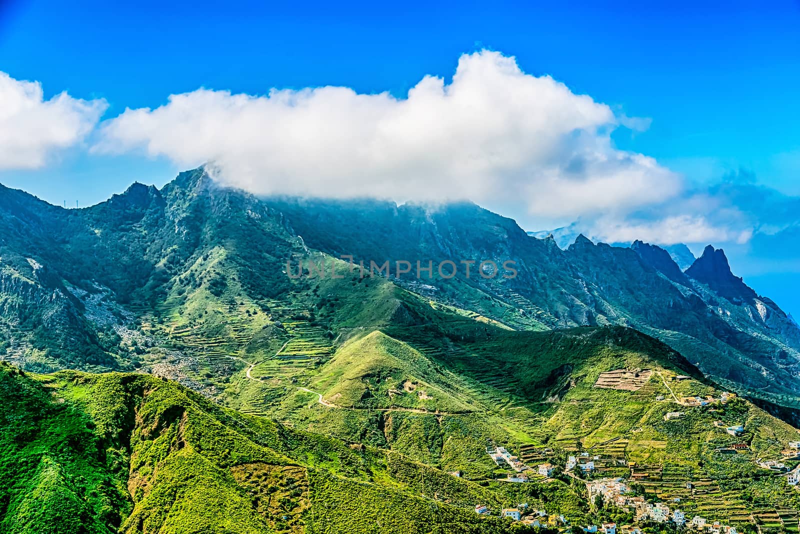 Clouds over the mountains on blue sky background with buildings in valley
