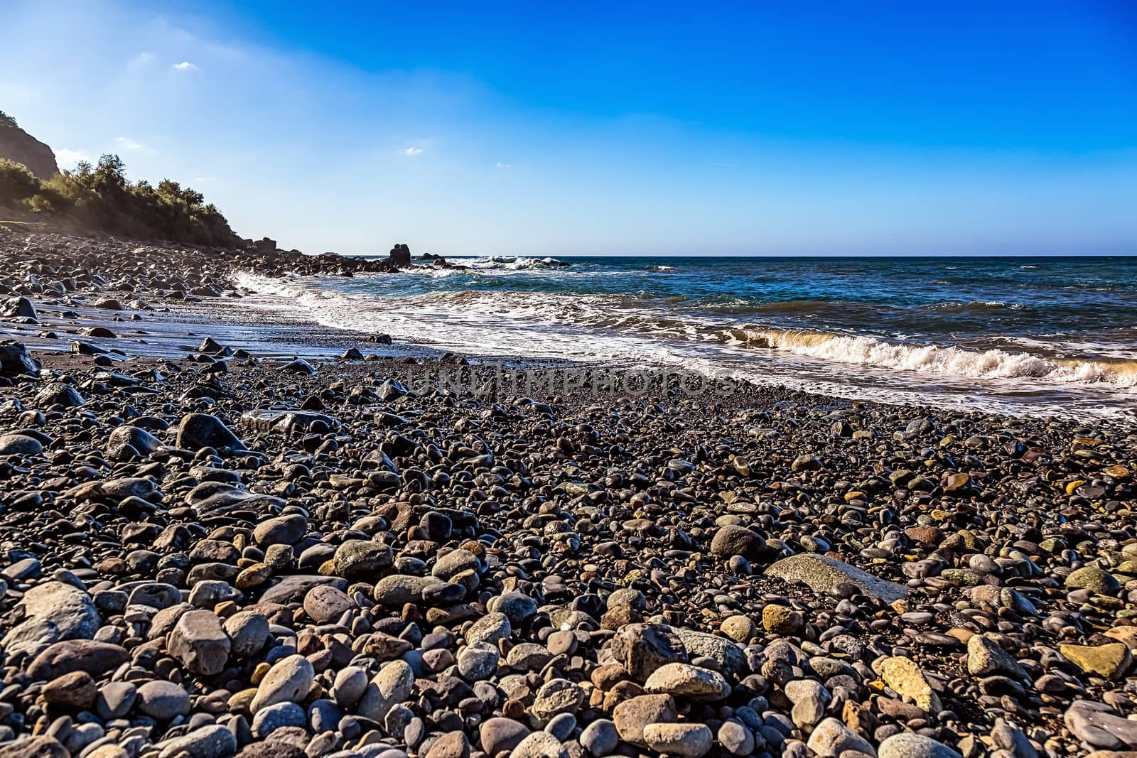Wild stone beach on coast of the Atlantic ocean with waves and sky with clouds and skyline or horizon in Tenerife Canary island, Spain at spring or summer